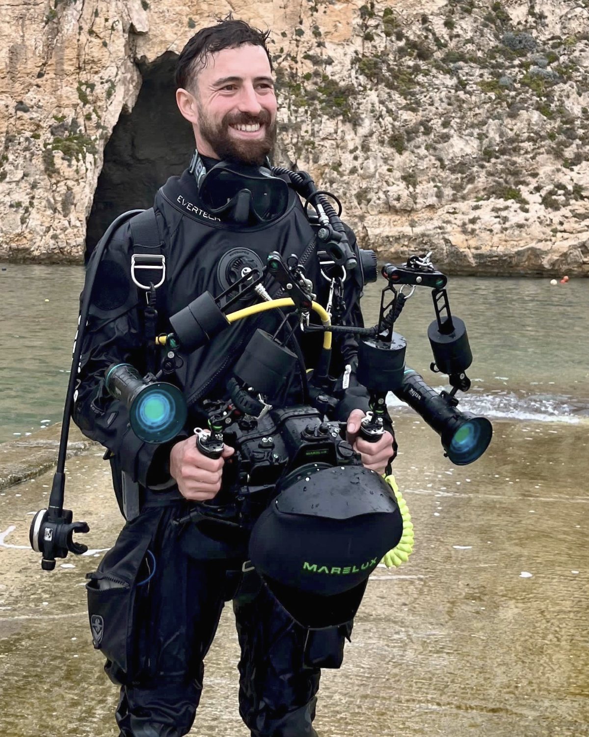 Sam Bard in a drysuit holding his underwater camera rig, Malta